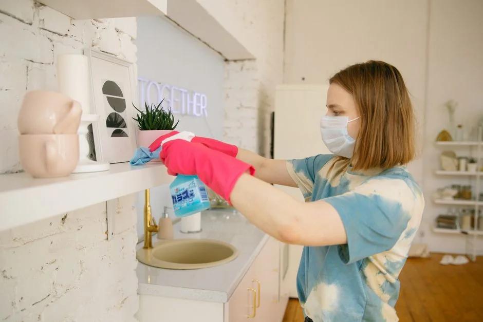 Two women in work clothes cleaning a modern living room using a vacuum and mop.